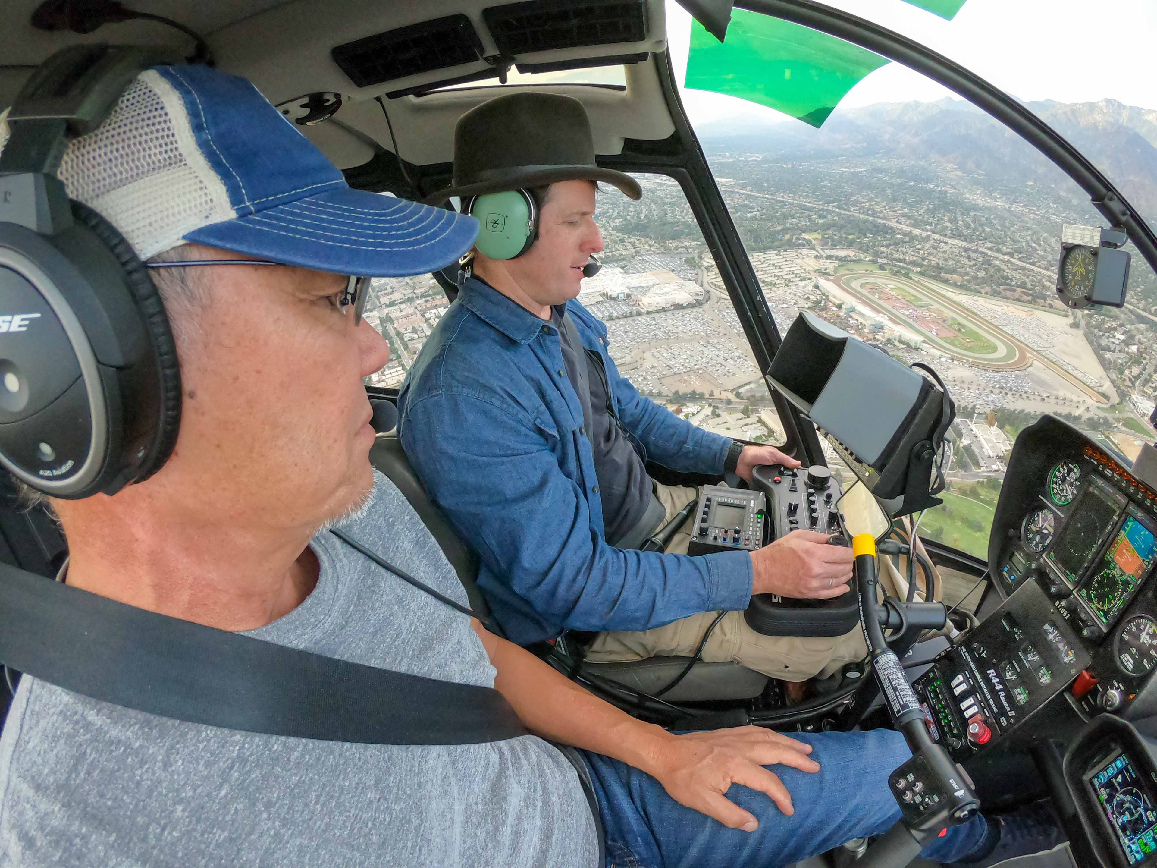 David Alan Arnold in cowboy hat operating camera controls in helicopter cockpit flying over horse racing track, Breeders Cup